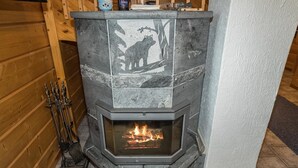 A stone fireplace with a fire burning inside, surrounded by wooden walls and a tiled floor.