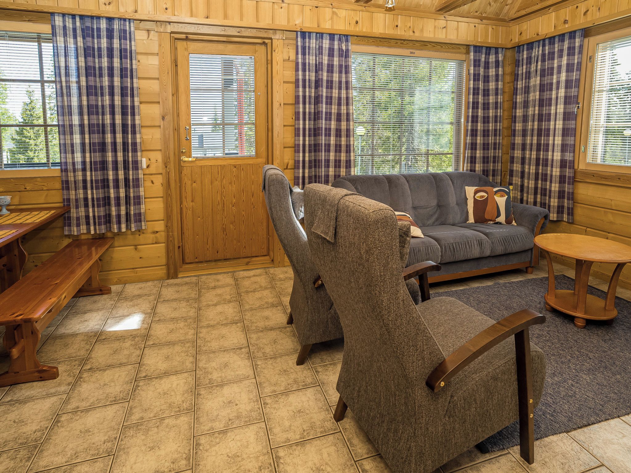 Ein gemütliches Blockhauss-Interieur mit einer Holztür, einer Couch, einem Sessel, einem kleinen Tisch und einer Bank.