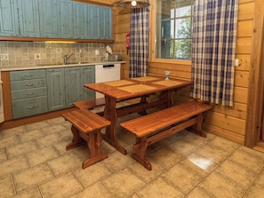 Una cocina con una mesa de madera y bancos, lavavajillas y una ventana con cortinas.