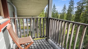 A wooden deck with a bench and a railing overlooking a forested area.