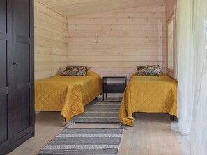 Una cabaña con dos camas, una mesita y un ventanal con cortinas.