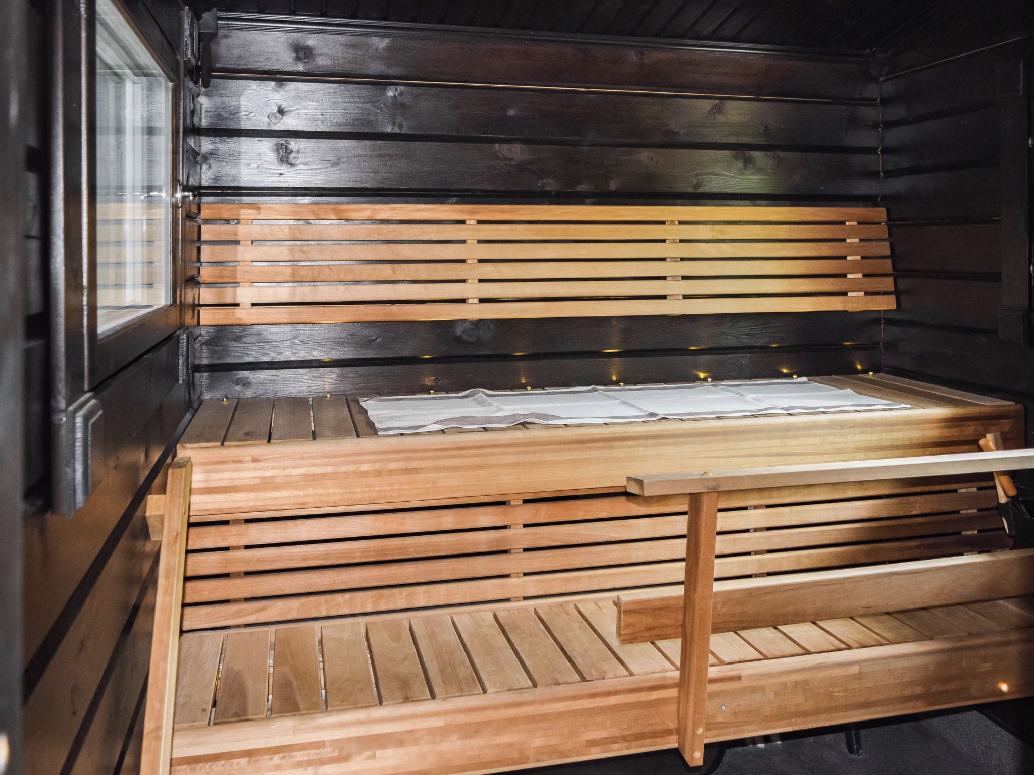 Een houten bank met een gesloten ribbenstructuur, geplaatst tegen een donkere houten wand.