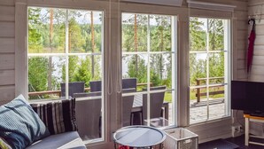 Une pièce confortable avec un canapé, une petite table ronde et un téléviseur. De grandes fenêtres offrent une vue sur une forêt et un lac.