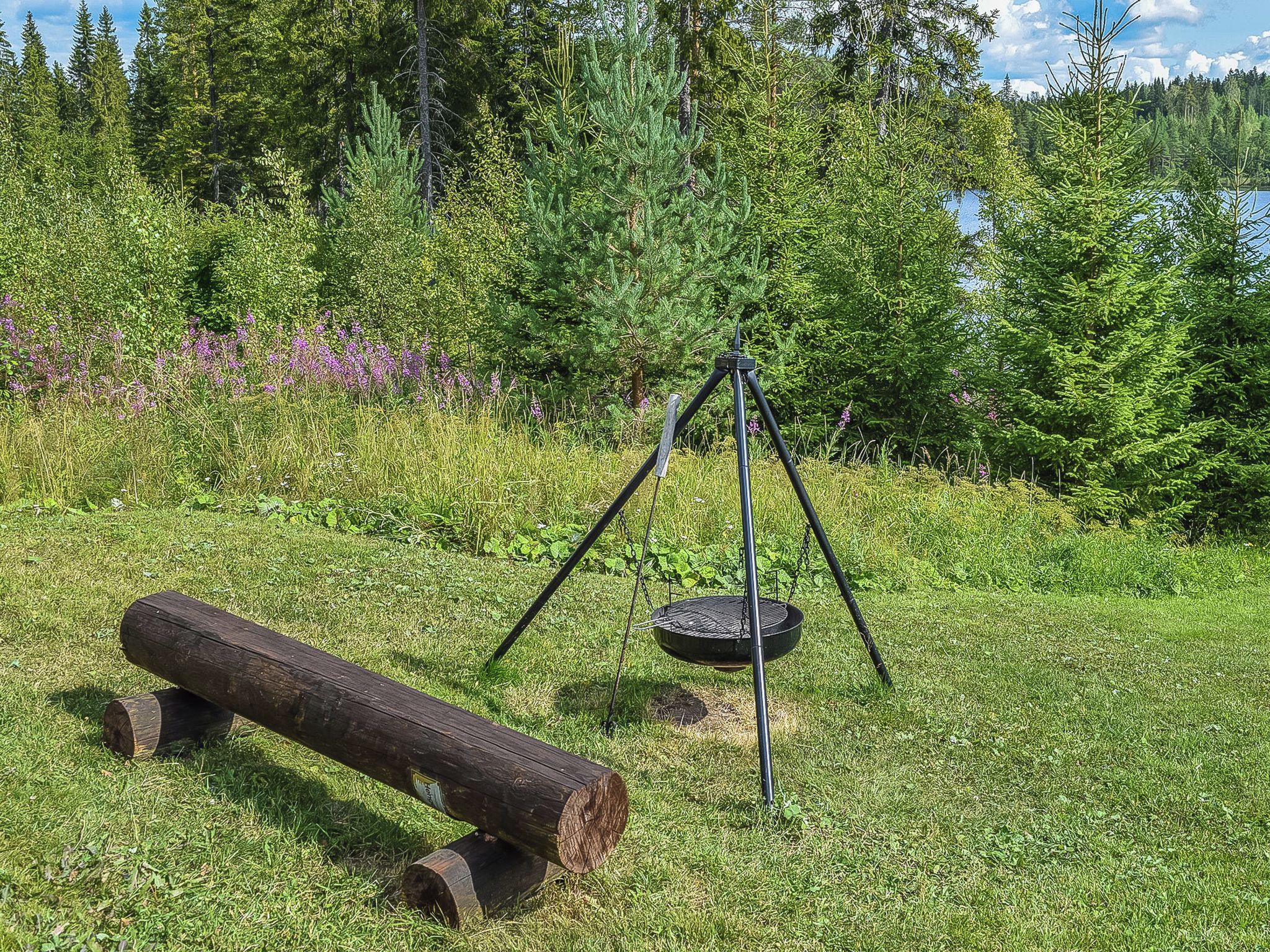 Ruohikkoalue ulkona, jossa on metallinen kolmijalkainen jalusta ja pyöreä grilli.