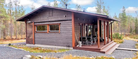 A cabin with a covered porch, large windows, and a gravel driveway.