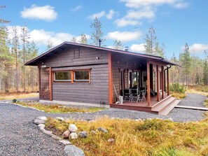 A cabin with a covered porch, large windows, and a gravel driveway.