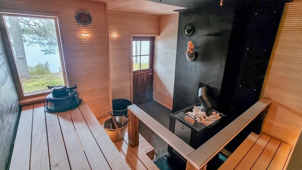 Una sauna amb exterior negre, terres de fusta i una finestra amb vista a un paisatge natural.