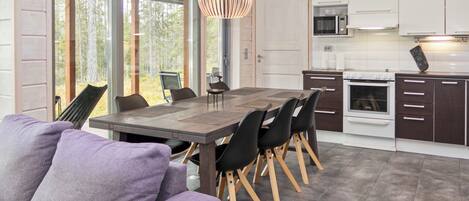 A modern kitchen with a dining area, featuring a large wooden table, black chairs, and a hanging light fixture.
