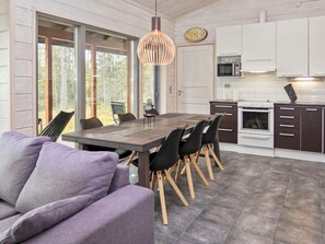 A modern kitchen with a dining area, featuring a large wooden table, black chairs, and a hanging light fixture. - Lumikukka by Interhome (Kuusamo)