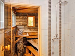 Bany d'una cabana de fusta amb dutxa, seients de fusta i una finestra.