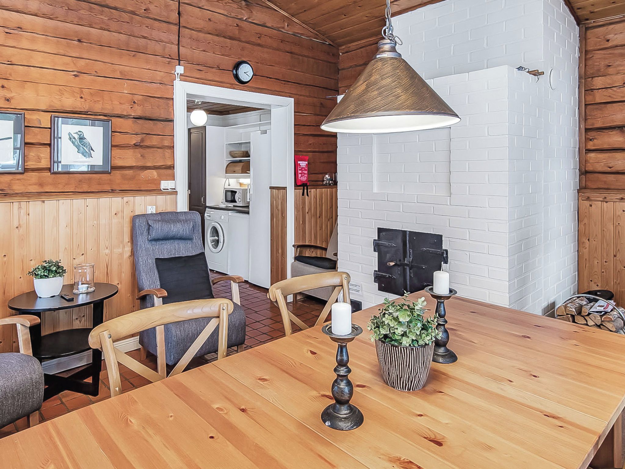 Un intérieur en bois avec une table à manger, des chaises, un luminaire suspendu et un mur en briques blanches.