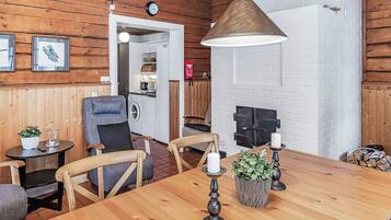 A wooden interior with a dining table, chairs, a hanging light fixture, and a white brick wall.