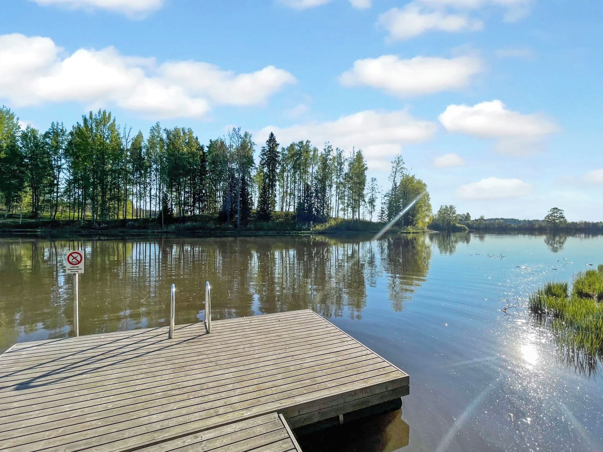 Une jetée en bois s’étendant sur un lac paisible, avec un ciel dégagé et des arbres en arrière-plan.