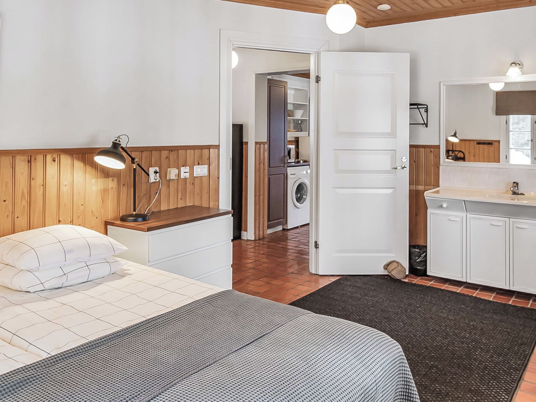 Une chambre à coucher avec un lit, une table de chevet, une lampe et une vue sur la cuisine.