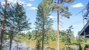 A lakeside cabin with a deck overlooking a calm lake, surrounded by tall trees and a clear sky. - Satakieli by Interhome (Somero)
