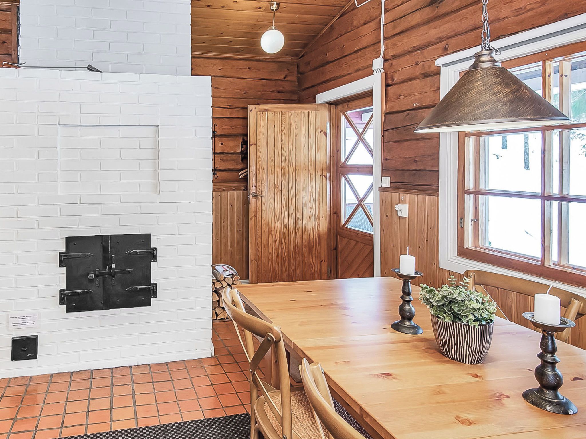 Un interior de madera con una pared de ladrillo, una puerta de madera, una mesa de comedor con sillas y una lámpara colgante.