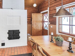 A wooden interior with a brick wall, a wooden door, a dining table with chairs, and a hanging light fixture.