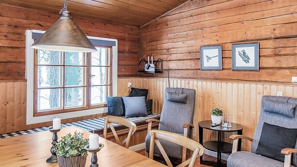 A cozy cabin interior with a wooden dining table, two chairs, a sofa, and a hanging light fixture. - Satakieli by Interhome (Somero)
