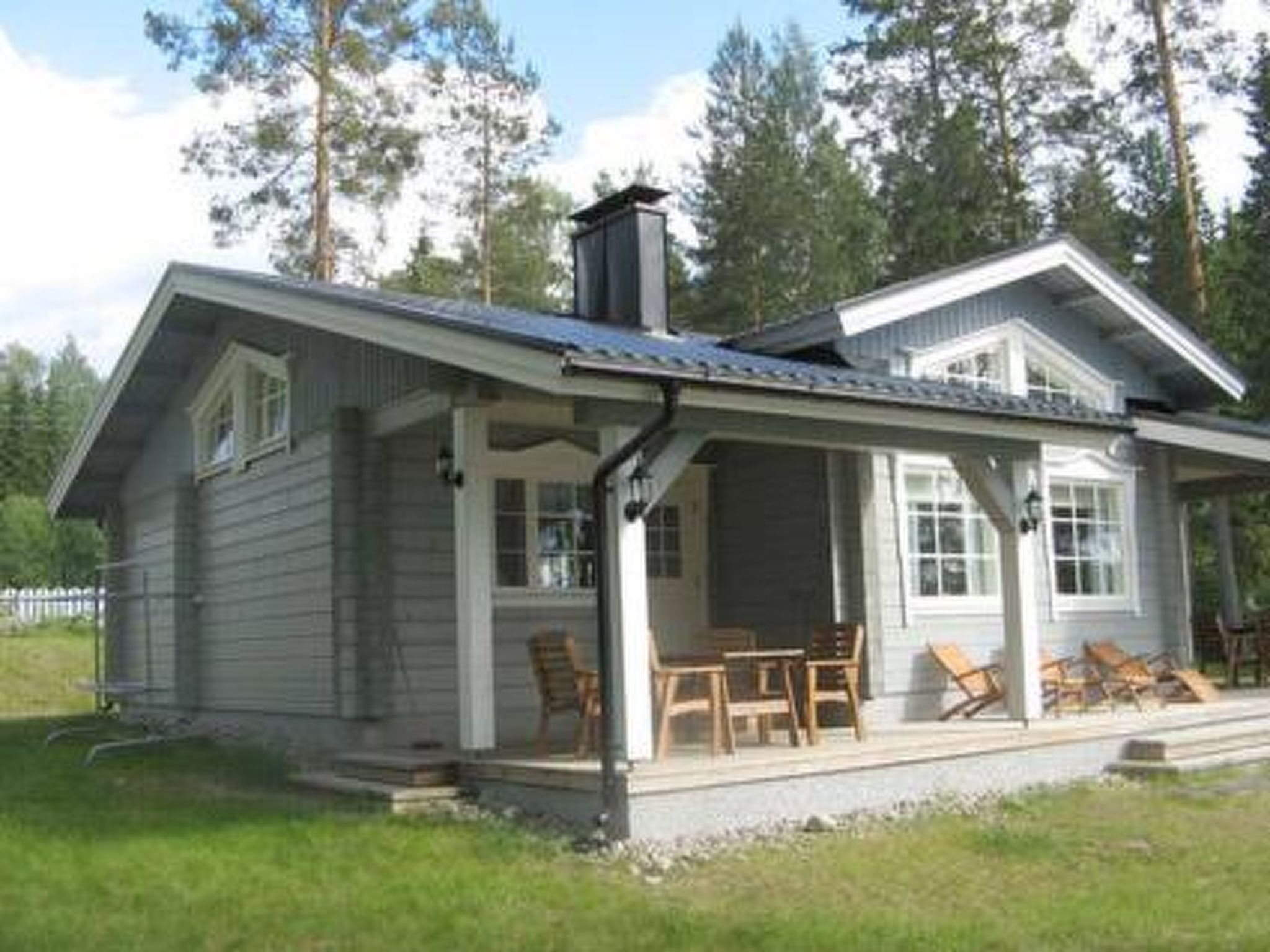 Een houten chalet met twee verdiepingen, een overdekte veranda en een schoorsteen.