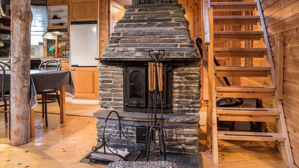 A cozy cabin interior with a stone fireplace, wooden walls, a dining area, and a wooden staircase. - Ylläsparit as. 2 by Interhome (Ylläsjärvi)