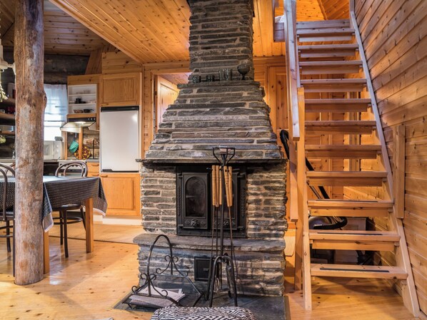 A log cabin interior with a stone fireplace, wooden staircase, and a dining area.