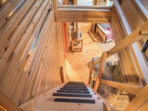 A wooden staircase leading to a loft bedroom with a bed and a small table.