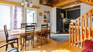 A spacious dining area with a wooden table and chairs, a kitchen with modern appliances, and a wooden staircase.