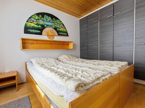 Quarto com cama de madeira, guarda-roupa e prateleira na parede com um quadro.
