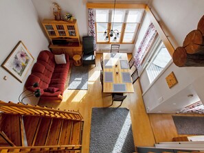 Ampla sala de estar com sofá vermelho, mesa de jantar de madeira e escada que leva a um andar superior.