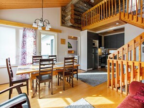 A spacious dining area with a wooden table and chairs, a staircase leading to an upper level, and a kitchen in the background.