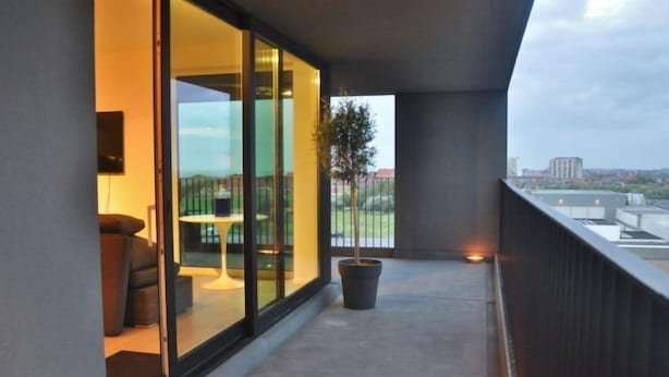 Varanda com porta de vidro que dá para um quarto, planta em vaso e vista da paisagem urbana.