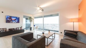Uma sala de estar moderna com sofás cinzas, uma mesa de centro e uma TV fixada na parede.