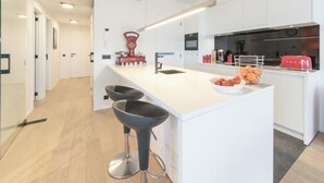 Uma cozinha moderna com armários brancos, uma ilha central com banquetas, uma balança vermelha e uma torradeira.