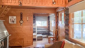 Ein gemütliches Blockhaus-Interieur mit Holzvertäfelung, Kamin, einer Couch und Blick ins Freie.