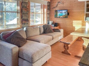 Una sala de estar acogedora con un sofá seccional, una mesa de comedor de madera y un televisor en la pared.