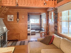 Ein gemütliches Blockhaus-Interieur mit Holzausbau, Kamin, einer Couch und Blick durch das Fenster.