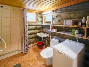 Ein Badezimmer im Blockhausstil mit Dusche, Toilette, Waschbecken und Waschmaschine.