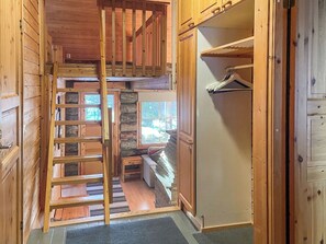 Interior de madera con un entrepiso para dormir, un armario con espacio para colgar ropa y una pequeña zona de estar con un banco.