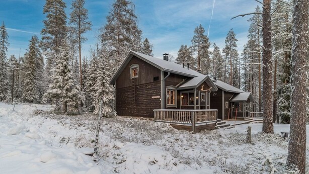 A wooden cabin with a porch, surrounded by snow-covered trees.