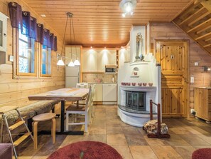 A cozy cabin interior with a wooden dining area, a kitchen with a built-in stove, and a fireplace.