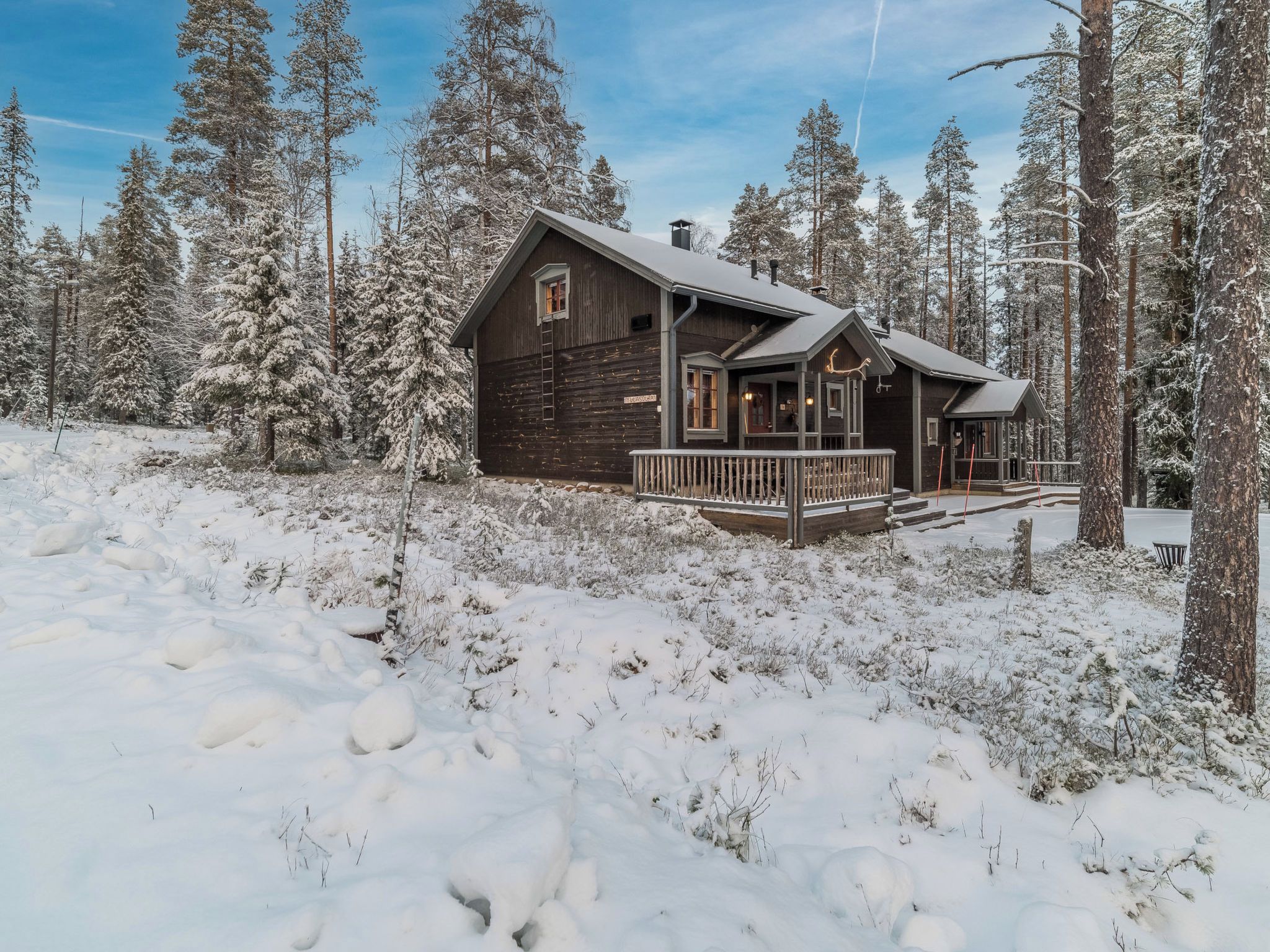 A wooden cabin with a porch, surrounded by snow-covered trees.