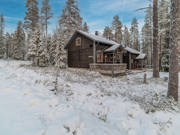 A wooden cabin with a porch, surrounded by snow-covered trees.