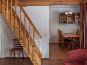 A wooden staircase leading to a dining area with a table and chairs, a red sofa, and a kitchen area with shelves. - Peiponpesä b by Interhome (Nilsiä)