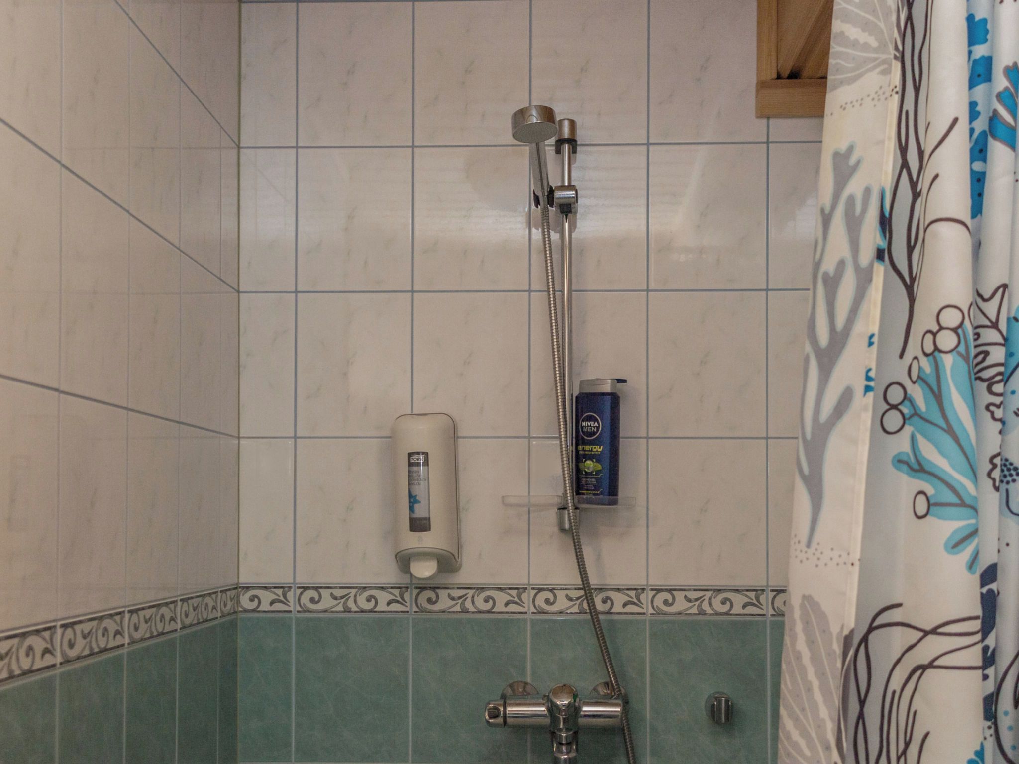 Un baño con ducha, dispensador de jabón y secamanos.