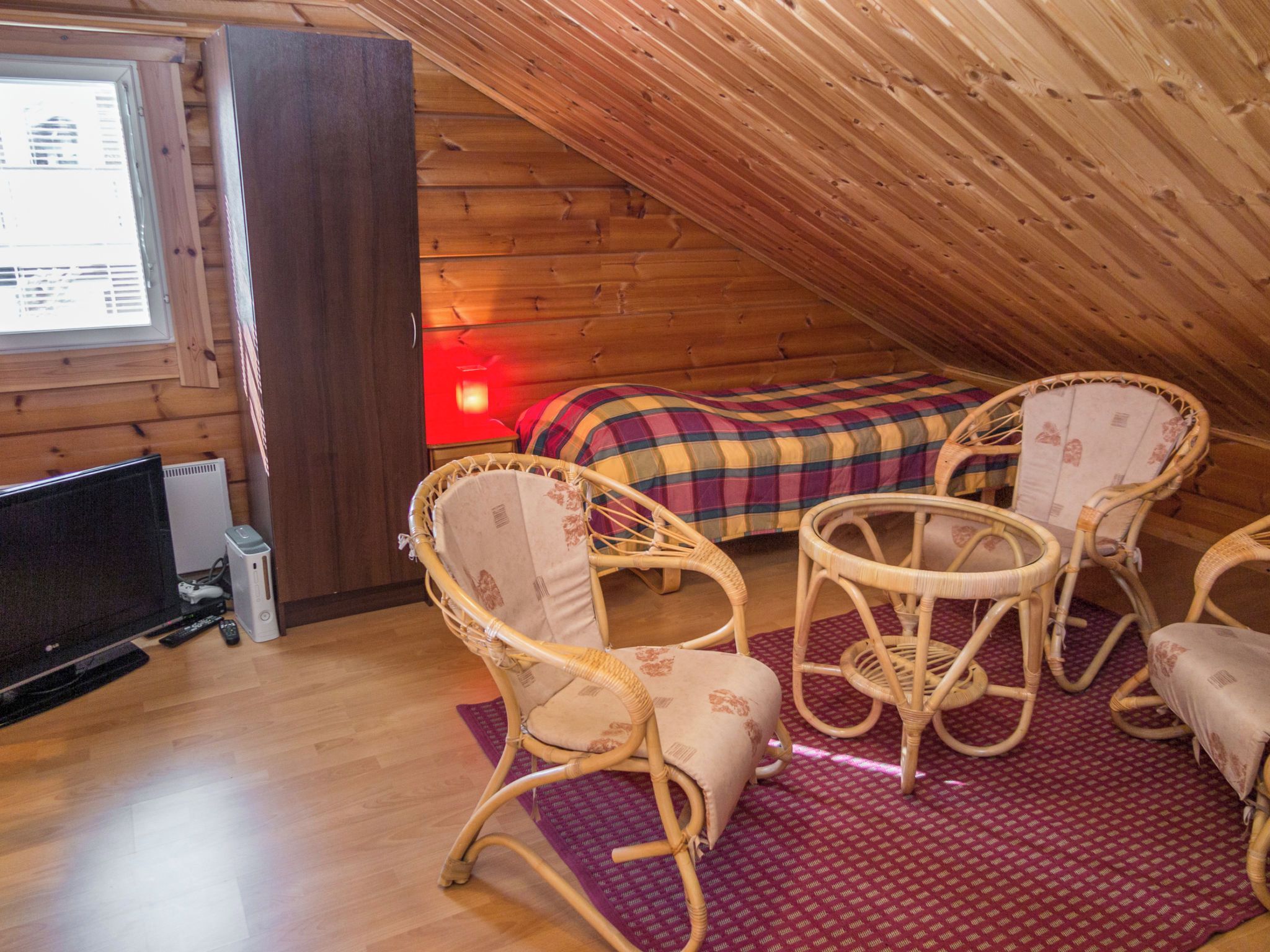 Ein gemütliches Schlafzimmer im Dachgeschoss mit einem Bett, zwei Korbstühlen, einem Fernseher und einem Fenster.