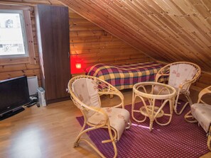 Quarto de sótão aconchegante com cama, duas cadeiras de vime, uma televisão e uma janela.