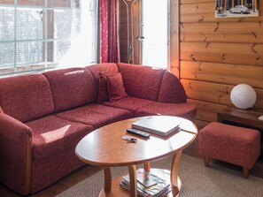 Uma sala de estar acolhedora com um sofá vermelho estampado, uma mesa de centro de madeira e um pequeno banquinho.