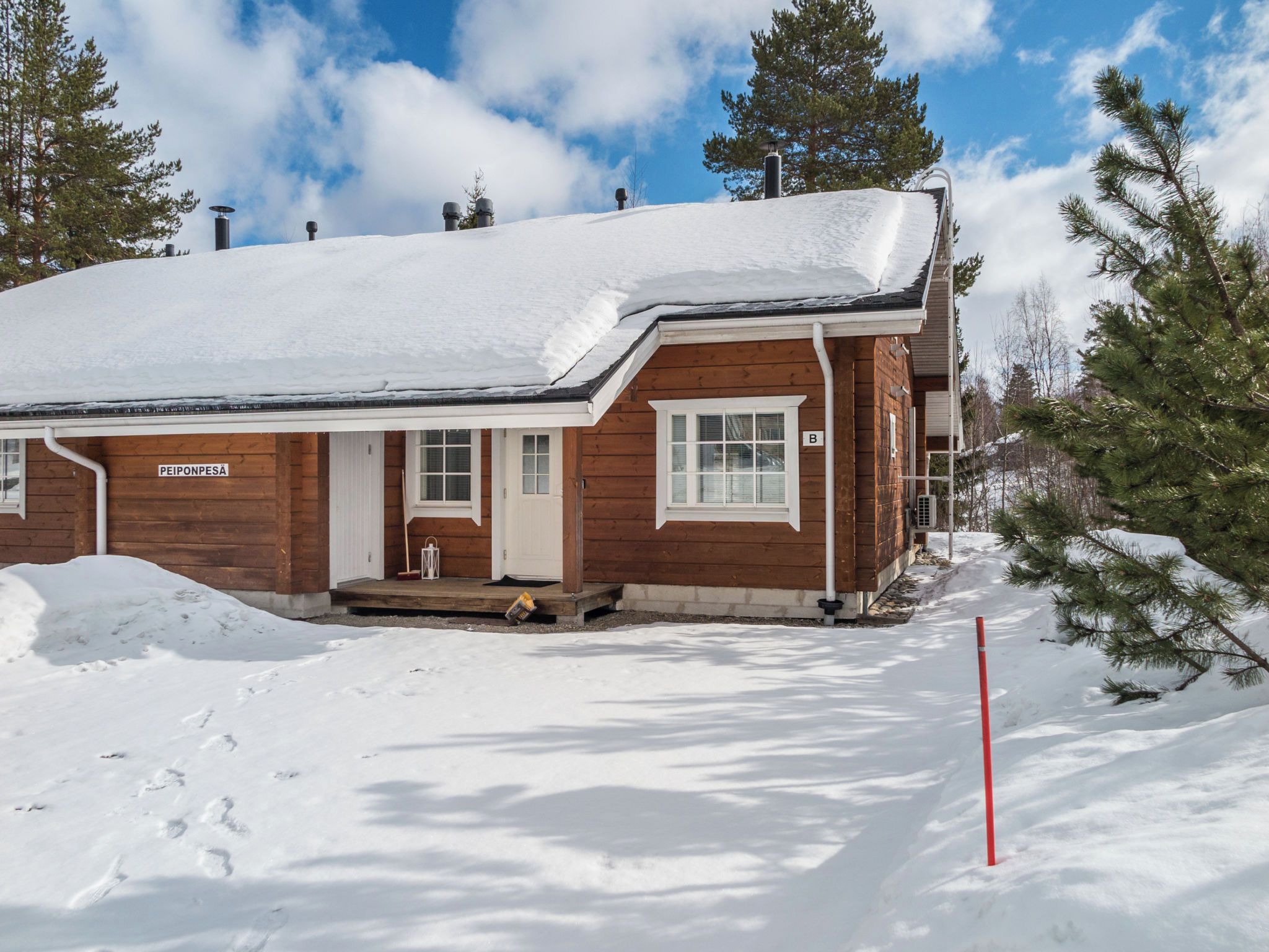 Una cabaña de madera con techo nevado, una chimenea visible y un letrero que dice 'PEIPONPESÁ'.