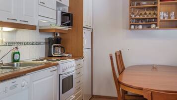 Eine kompakte Küche mit weißen Schränken, einer Mikrowelle, einer Kaffeemaschine und einem Esstisch mit Stühlen.