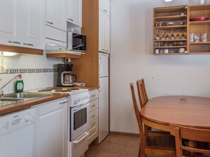 Cozinha compacta com armários brancos, micro-ondas, cafeteira e mesa de jantar com cadeiras.